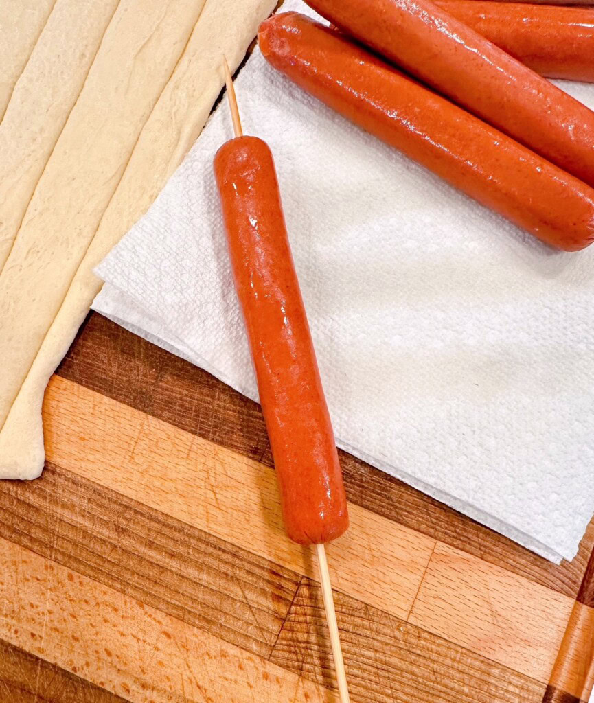 Placing skewer through the hot dog.