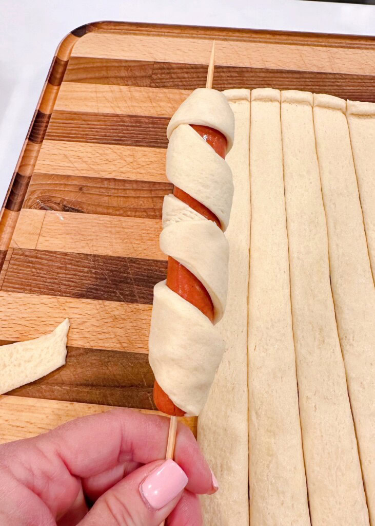Wrapping crescent dough around a hot dog.