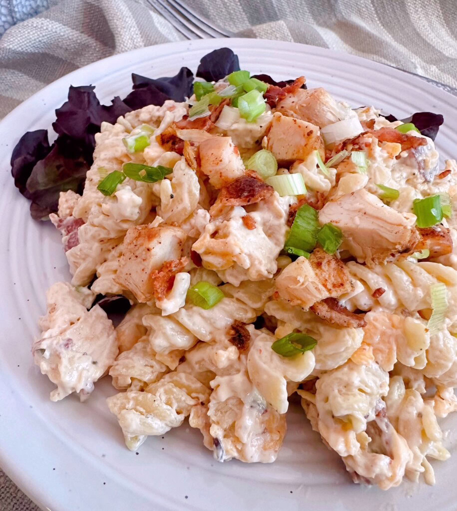 Close-up photo of Chicken Bacon Pasta salad on a bed of red leaf lettuce.