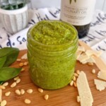 Pesto sauce in a jar on a small wooden cutting board.