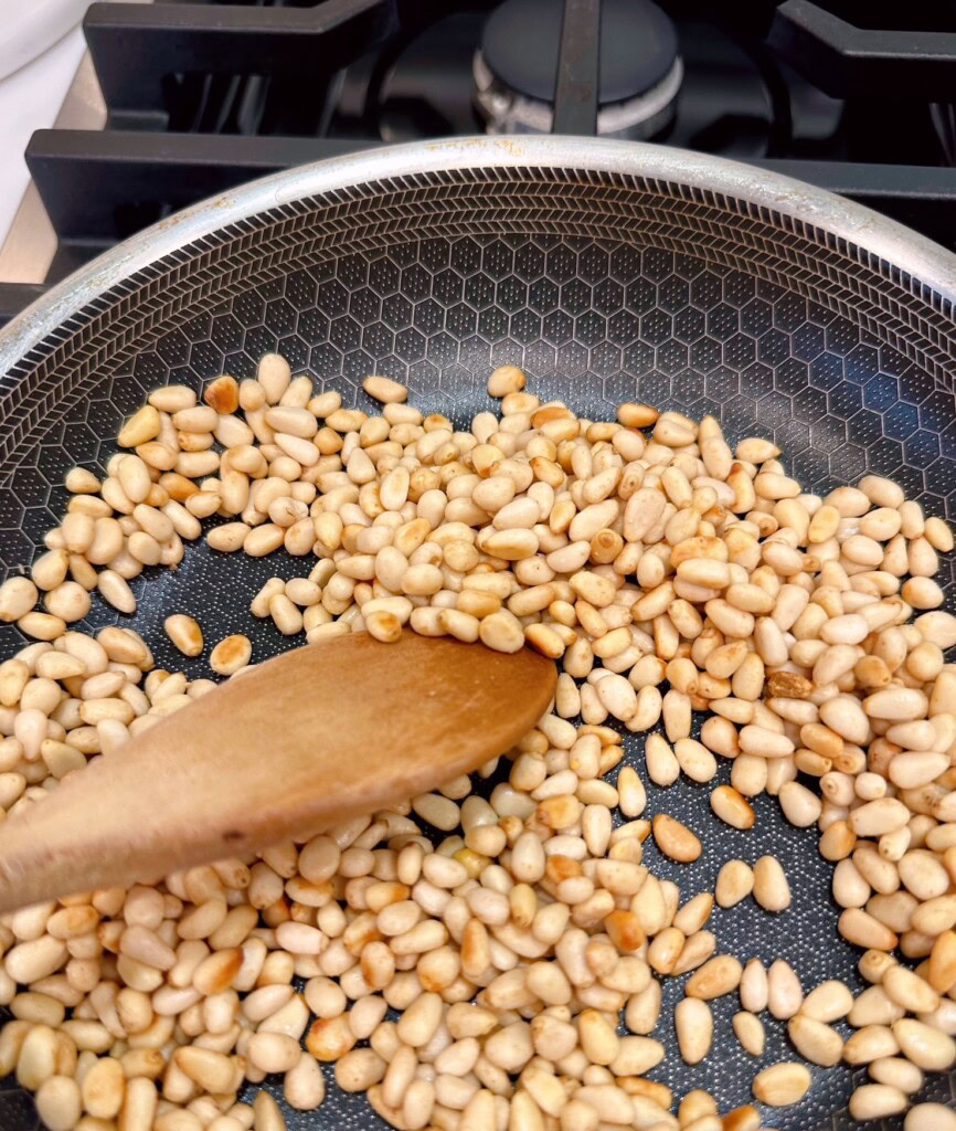 Stirring pine nuts in small skillet over medium heat.