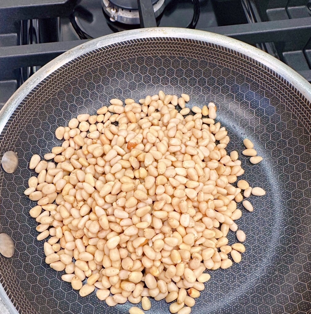 Pine nuts in a small skillet on the stove top.