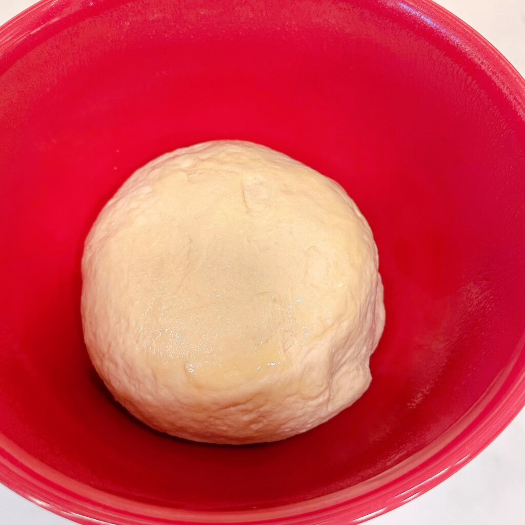 Dough shaped into a large ball and placed in a oiled bowl.