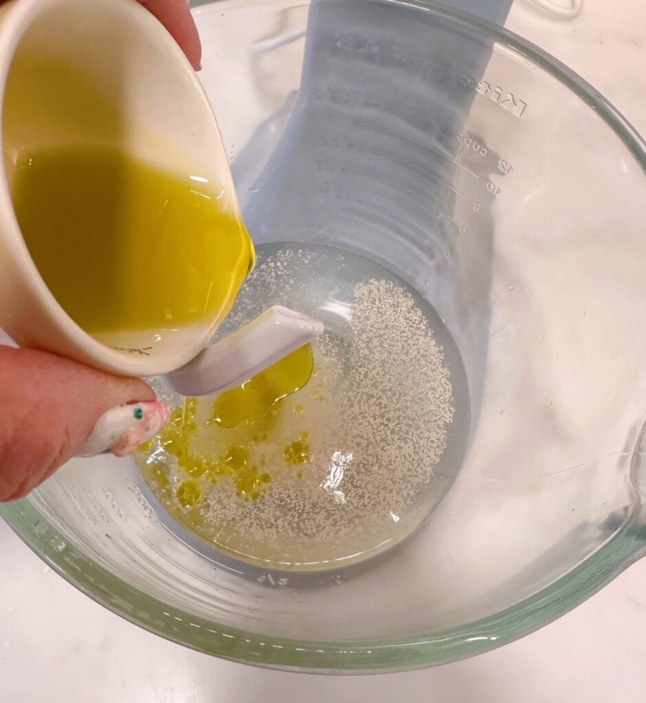 Adding olive oil to water, yeast and salt.