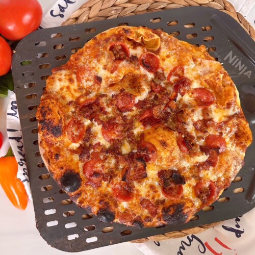Oven baked pizza crust with all meat toppings on a pizza paddle.