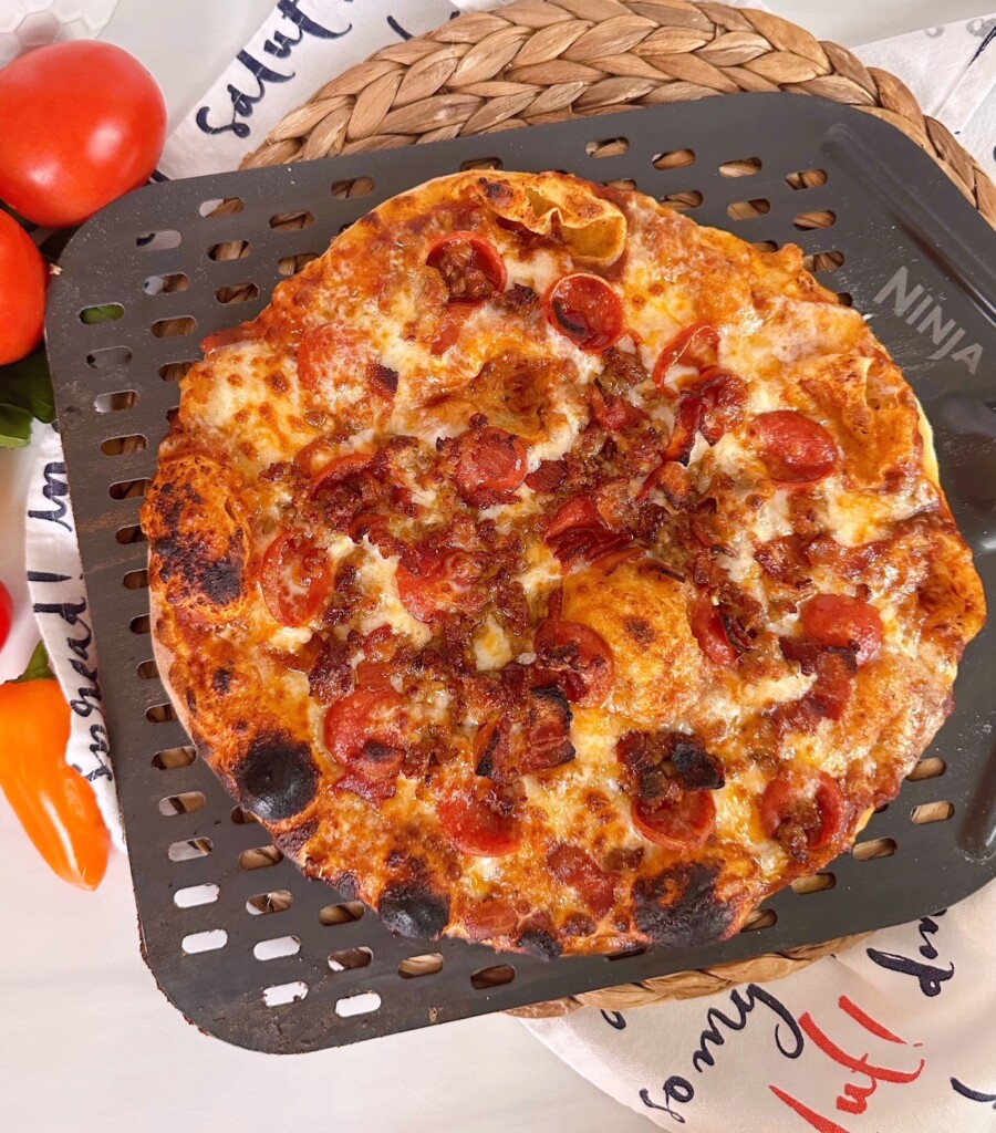 Oven baked pizza crust with all meat toppings on a pizza paddle.