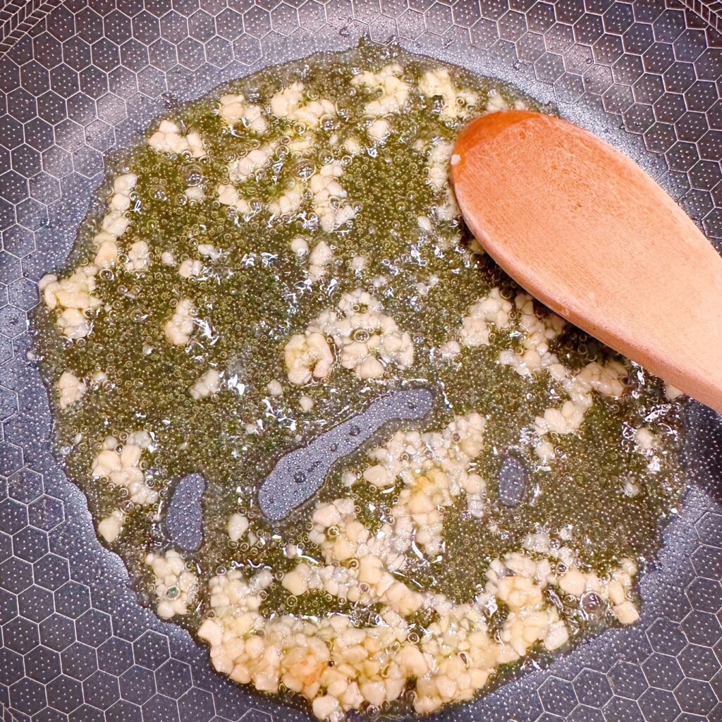 Sauteeing garlic in olive oil in a small skillet on the stovetop.