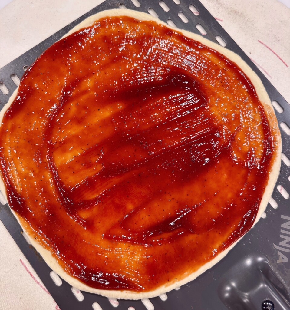 BBQ sauce spread evenly over pizza crust.