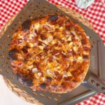 BBQ Cowboy Chicken and Bacon Pizza on a pizza wheel with a red and white checkered cloth.