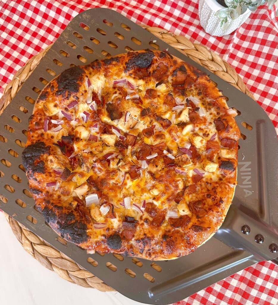 BBQ Cowboy Chicken and Bacon Pizza on a pizza wheel with a red and white checkered cloth.