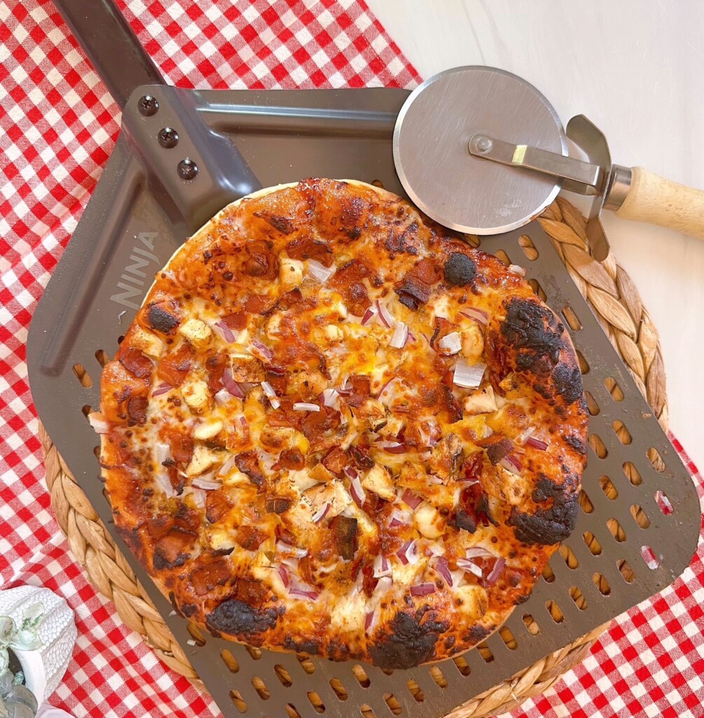BBQ Chicken and Bacon Pizza on a pizza paddle with a pizza wheel.
