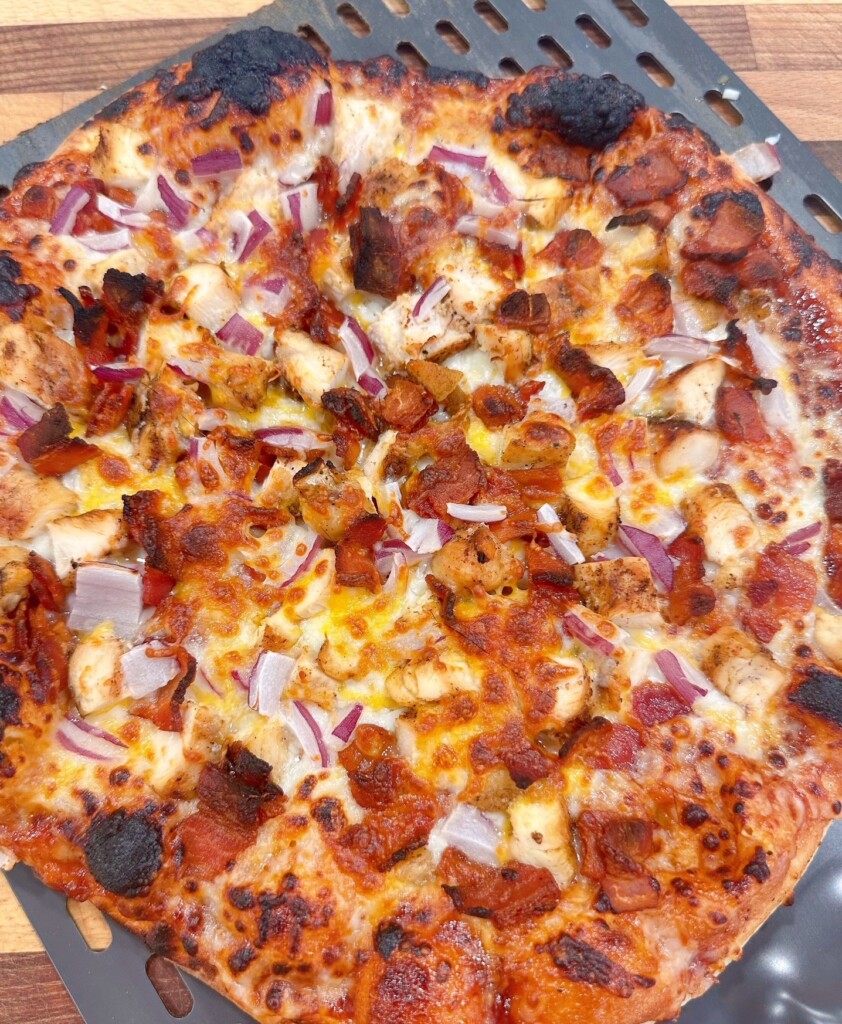 Baked pizza coming out of the oven and placed on a cutting board.