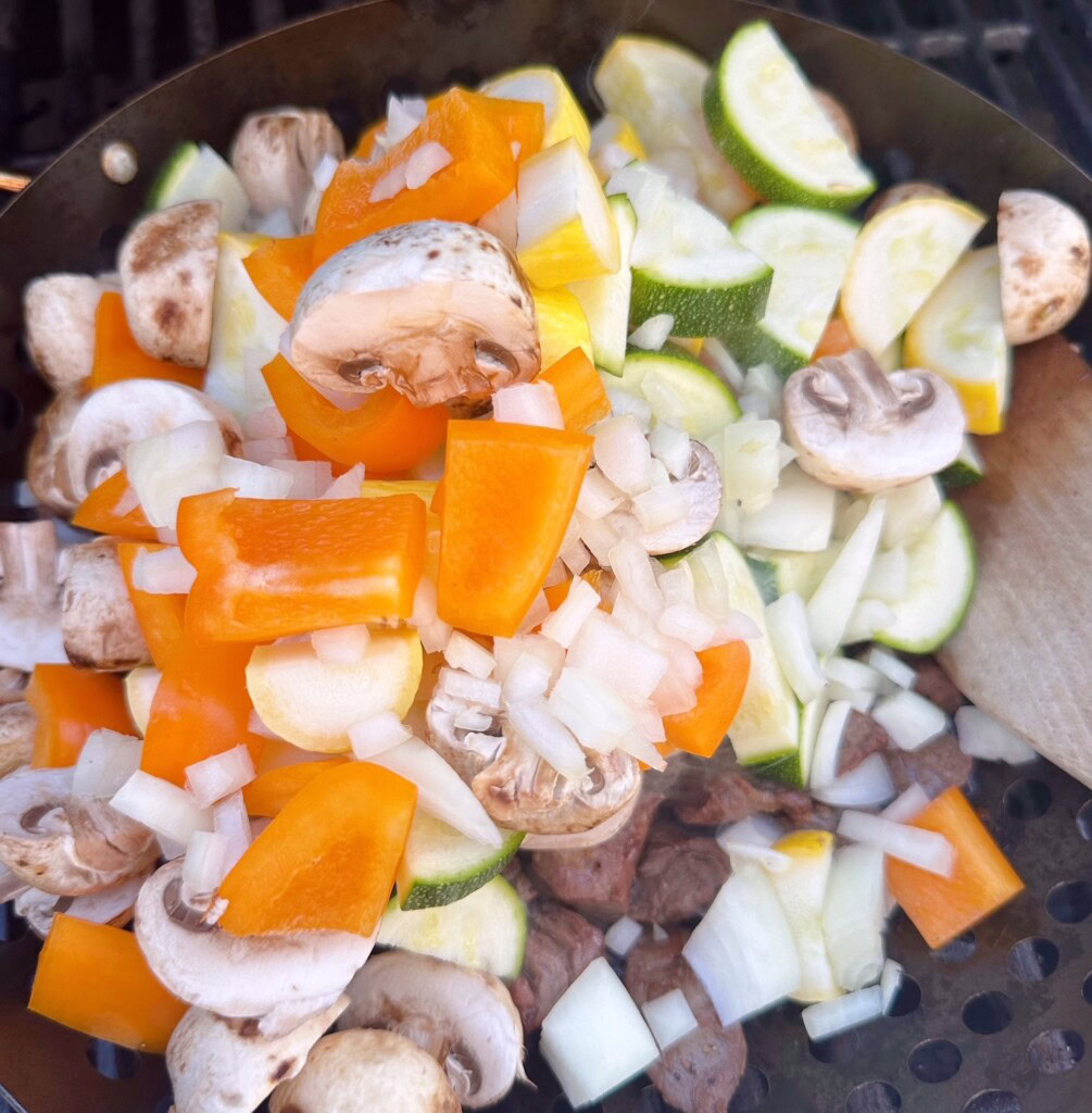 Adding the cut up raw vegetables to the steak.