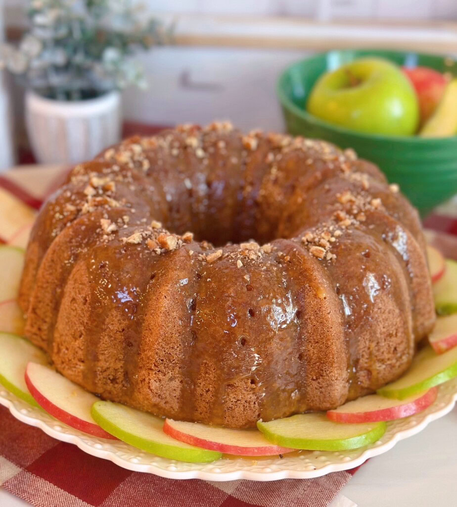Apple Cake with Caramel Glaze on a cake plate surrounded by apple slices.