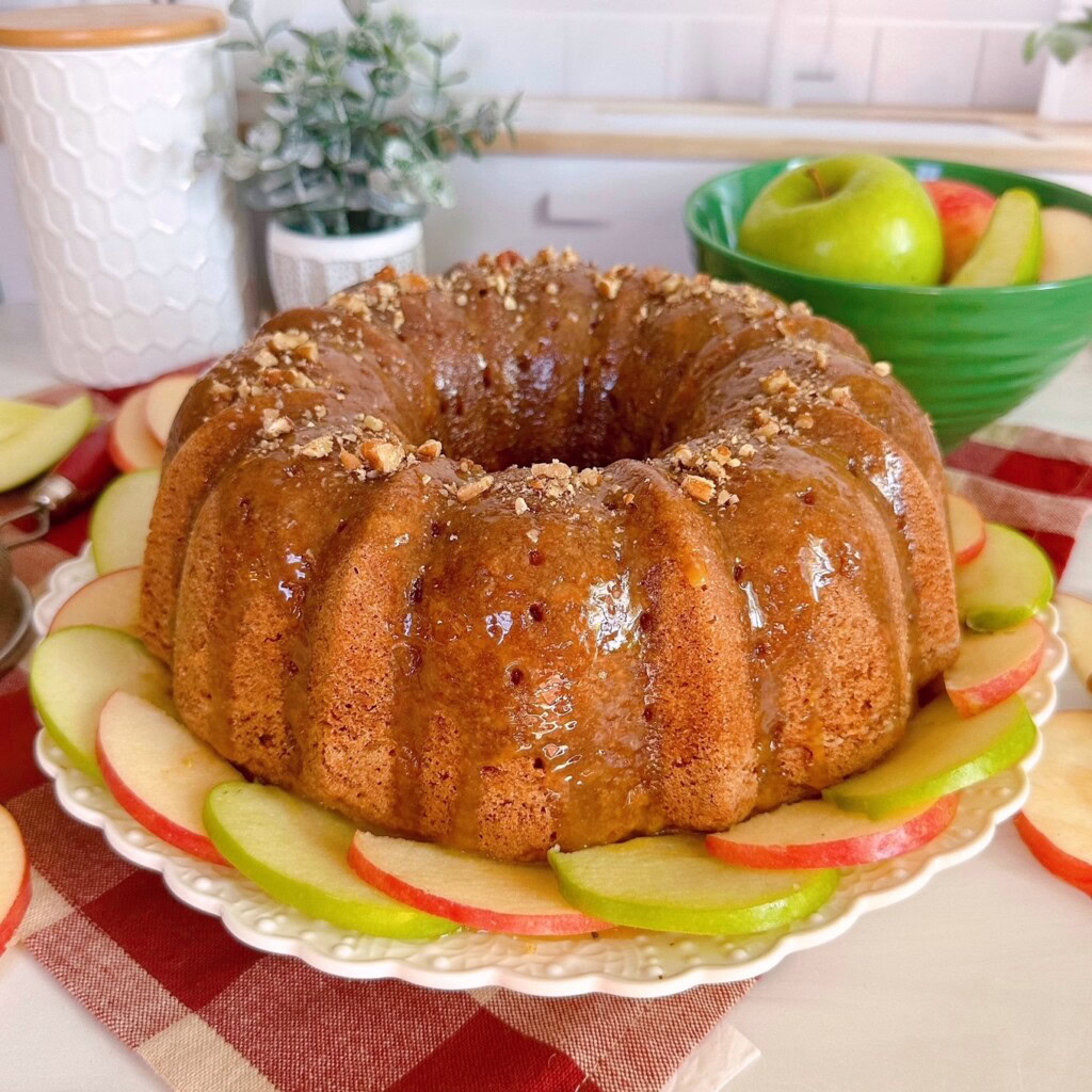 Easy Apple Cake with caramel glaze on a cake plate surrounded by the apples.