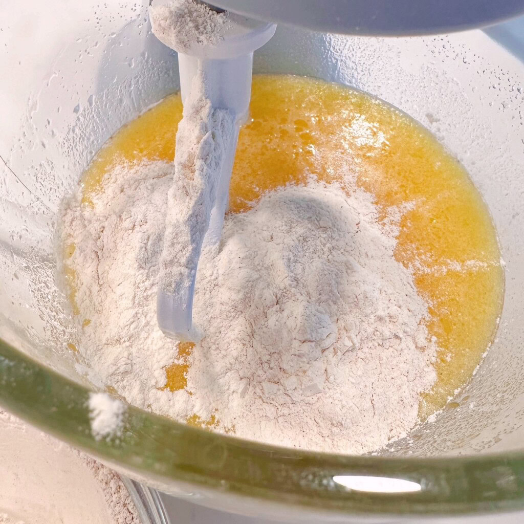 Adding dry ingredients to wet ingredients in the bowl of the mixer.