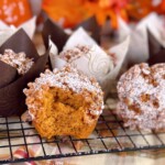 Pumpkin ginger streusel muffins on a cooling rack with one muffin with a bite out of it.