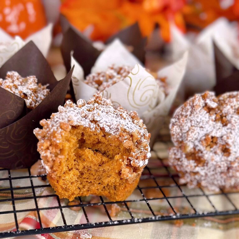 Pumpkin ginger streusel muffins on a cooling rack with one muffin with a bite out of it.