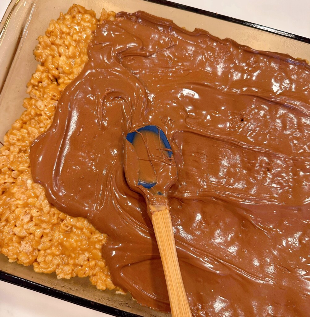 Spreading the melted chocolate chips on top of the rice krispie bars.